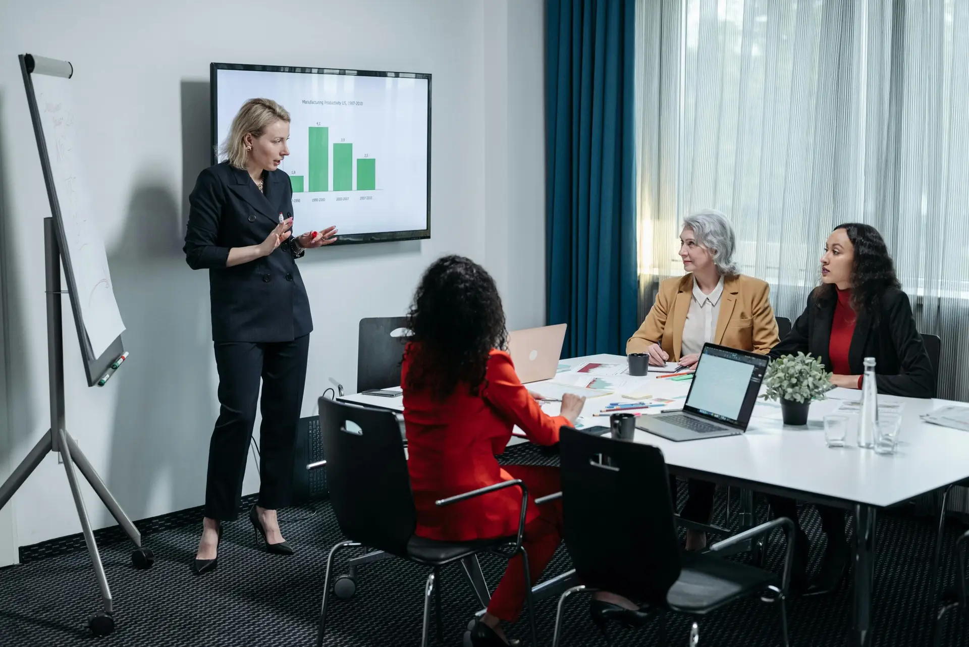 A group of professional women engaged in a business presentation in a modern conference room.